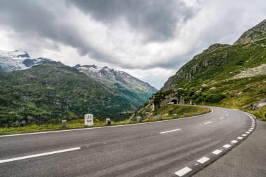 İsviçre Alpleri 'nde ortasında beyaz bir çizgi olan bir yol. Yol bomboş. Gökyüzü bulutlu.