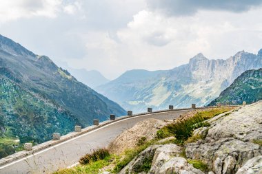 Çimenli yamaçlı bir yol ve İsviçre Alplerinde arka planda bir dağ. Yol ağaçlarla kaplı ve üzerinde beyaz bir çizgi var.