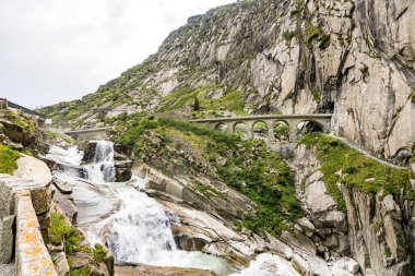 İsviçre Alpleri 'nde içinden nehir akan bir dağ sırası. Nehir yeşil ağaçlarla çevrilidir. Dağlar karla kaplı. Şeytanın köprüsü