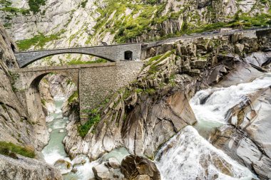 İsviçre Alpleri 'nde içinden nehir akan bir dağ sırası. Nehir yeşil ağaçlarla çevrilidir. Dağlar karla kaplı. Şeytanın köprüsü
