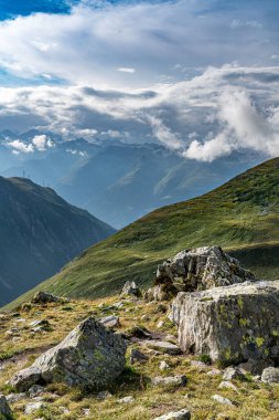 İsviçre Alplerinde bulutlu bir gökyüzü olan bir dağ sırası. Bulutlar beyaz ve gri. Dağlar yeşil çimlerle kaplıdır.
