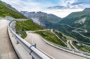 İsviçre Alpleri 'nde önünde yol olan bir dağ sırası. Yol boş ve ortada beyaz bir çizgi var.