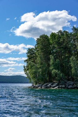 island of faith lake turgoyak ural in russia. A body of water with a forest in the background. The water is blue and calm. There are some birds flying over the water