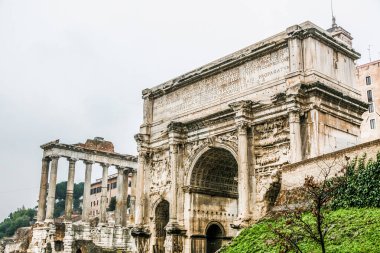 Roma İtalya 'sında arkasında bir bina bulunan büyük bir kemer yolu. Kemer yolu beyaz ve çok detay içeriyor.