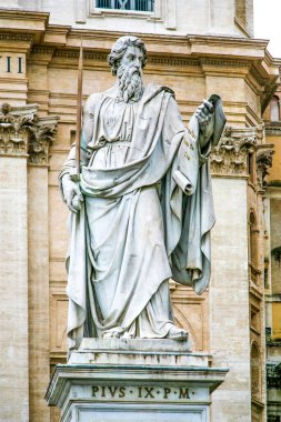 Elinde kitap tutan bir adamın heykeli. Heykelin adı Pius IX. Heykel beyazdır ve bir binanın önündedir.