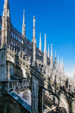Milano İtalya 'da Duomo. Tepesinde bir sürü heykel olan bir sıra bina. Binalar beyaz ve gökyüzü mavi.