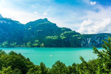 İsviçre Alplerinde arka planda dağ olan güzel bir göl. Su mavi ve gölde birkaç yelkenli var.