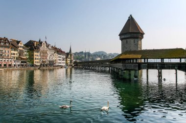 Lucerne İsviçre 'de arka planında bir bina olan bir su birikintisinin üzerinde köprü. Köprü tahta ve çatısı var.