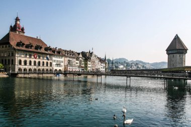 İsviçre 'de bir Luzern şehri. Nehir üzerinde köprüsü ve büyük bir binası var. Etrafta dolaşan bir sürü insan var.