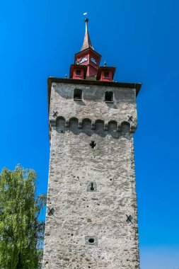 Lucerne İsviçre 'nin tepesinde kırmızı çatılı ve saati olan uzun bir kule. Kule ağaçlarla çevrili.