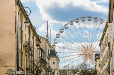 Büyük bir dönme dolap şehir sokağının ortasında. Sokak binalarla dolu ve birkaç sokak lambası var.