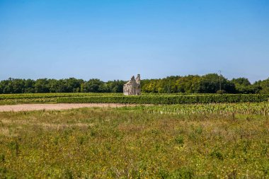 Fransa 'da büyük bir taş yapı bir tarlanın ortasındadır. Alan yeşil ve arka planda birkaç ağaç var.