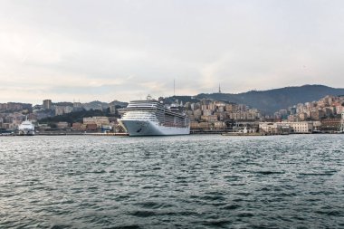 Akşamları İtalya 'nın Cenova limanında büyük bir çok katlı yolcu gemisi duruyor. Şehrin küçük bir kısmı arkadan görülebilir.