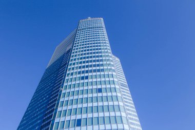 Arka planda mavi gökyüzü olan yüksek bir bina. Bina çok yüksek ve birçok penceresi var.