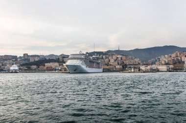 Akşamları İtalya 'nın Cenova limanında büyük bir çok katlı yolcu gemisi duruyor. Şehrin küçük bir kısmı arkadan görülebilir.