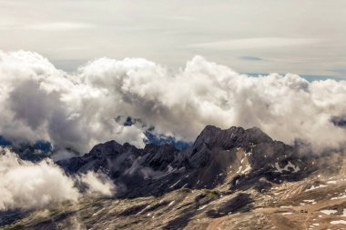 Almanya 'daki Zugspitze dağlarından gökyüzünde bulutlar görünen bir dağ silsilesi. Bulutlar beyaz ve kabarık. Dağlar karla kaplı.