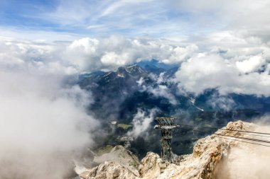 Dağın tepesinde uzun metal bir araba desteği var. Yapı bulutlarla çevrilidir. Bulutlar beyaz ve kabarık.
