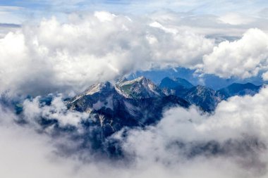 Almanya 'daki Zugspitze dağlarından gökyüzünde bulutlar görünen bir dağ silsilesi. Bulutlar beyaz ve kabarık. Dağlar karla kaplı.