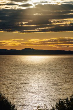 Üzerinde güneş parlayan büyük bir su kütlesi. Güneş gökyüzünde ve su da sakin. İtalya 'nın Umbria bölgesinde Trasimeno Gölü' nde bir akşam