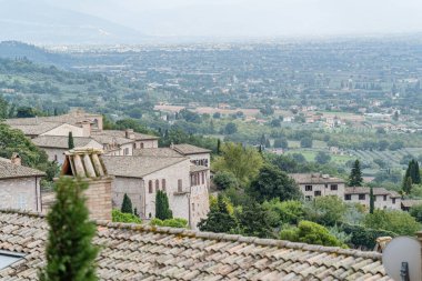 İtalya 'nın Assisi şehrinde birçok evi ve büyük bir tepesi olan bir şehir manzarası Umbria. Evlerin hepsi farklı boyutlarda ve yayılmış durumda.