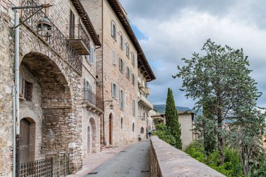 İtalya 'nın Assisi şehrinde önünde balkon ve ağaç olan taştan bir bina. Umbria. Bina eski ve kırsal bir cazibesi var. Balkon demirle döşenmiş.