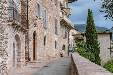 İtalya 'nın Assisi şehrinde önünde balkon ve ağaç olan taştan bir bina. Umbria. Bina eski ve kırsal bir cazibesi var. Balkon demirle döşenmiş.