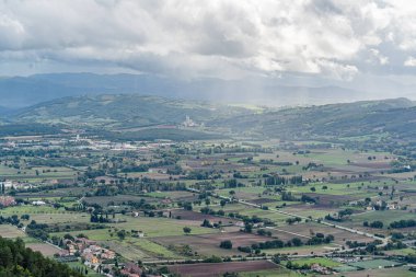Gubbio Bakış açısı İtalya Umbria 'da birkaç evi olan büyük bir tarla. Gökyüzü bulutlu. Gubbio İtalya 'da uzakta küçük bir kasaba var Umbria