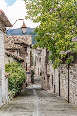 Gubbio İtalya 'da dar bir sokak. Sağında ağaç olan Umbria. Sokak binalarla dolu ve tavandan sarkan bir lamba var.