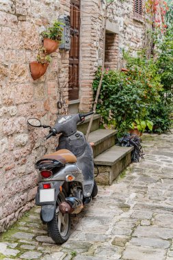 Gubbio, Umbria İtalya 'da bir kaldırım taşı caddesinde gri bir scooter park halinde. Scooter tuğladan duvara yaslanıyor.