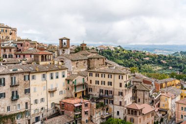 Ortada büyük bir bina bulunan Perugia İtalya 'nın Umbria kenti. Binanın saat kulesi var. Şehirde bir sürü bina var.