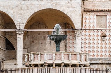 Perugia İtalya 'da Umbria' daki bir binanın önünde yeşil çanaklı bir çeşme var. Binanın bir sürü kemeri var ve taştan yapılmış.