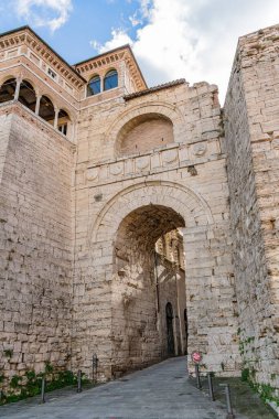 Perugia 'da Arco Etrusco adında balkonlu büyük bir taş bina. Kaldırımda bir insan yürüyor. Gökyüzü mavi