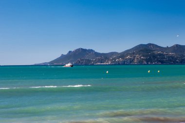 Cannes Fransa 'da bir dağın yakınında bir yelkenli yelkenli denize açılıyor. Gökyüzü açık ve su sakin.