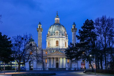 Viyana Avusturya 'da, tepesinde kubbe olan büyük beyaz bir bina gece aydınlanıyor. Bina ağaçlarla çevrili ve o bir kilise. Sahnenin huzurlu ve huzurlu bir havası var.