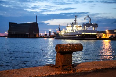 Hirtshals Danimarka 'daki bir rıhtıma büyük bir gemi yanaştı. Su sakin ve gökyüzü bulutlu.