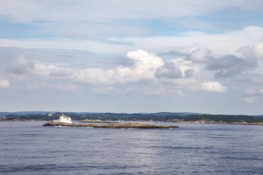 Norveç 'te önünde büyük bir su kütlesi bulunan küçük bir ada, uzaktan görülebilir. Gökyüzü bulutlu, ortama biraz karamsar bir hava katıyor.