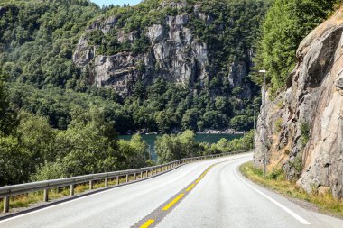 Norveç 'te üzerinde sarı çizgi ve tabela olan bir yol. Yol boş ve gökyüzü mavi.