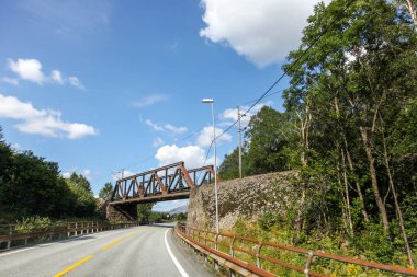 Norveç 'te üzerinde açık mavi bir gökyüzü olan bir köprü bir yolu kapsar. Köprü eski ve kırsal bir görünüme sahip.