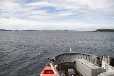 Norveç 'in fiyortlarında açık mavi gökyüzü olan bir tekne seyrediyor. Teknenin etrafı suyla çevrili ve etrafında uçan birkaç kuş var.