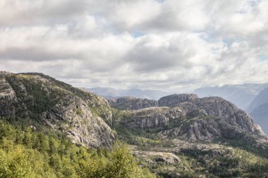 Dağlar Norveç 'te ağaçlar ve kayalarla kaplıdır ve gökyüzü bulutludur. Huzurlu ve huzurlu bir manzara. Dağlar ihtişam ve ihtişam hissi veriyor.