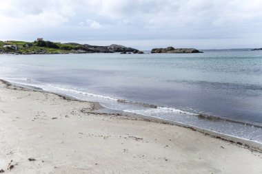 Norveç 'te kayalık bir kıyı şeridi ve uzakta küçük bir evi olan bir sahil. Gökyüzü bulutlu ve su sakin.