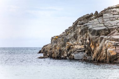 Norveç 'in arka planında büyük bir su kütlesi olan kayalık bir kıyı şeridi. Kayalar sahnenin her tarafına dağılmış, bazıları suya daha yakın, bazıları ise daha uzaklarda.