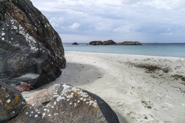 Norveç 'te kayalık bir plaj ve önünde büyük bir kaya var. Gökyüzü bulutlu ve su mavi.