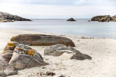 Norveç 'te kayalık bir plaj ve önünde büyük bir kaya var. Gökyüzü bulutlu ve su mavi.