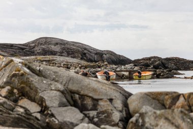 Norveç 'te kayalık bir kıyıda iki küçük tekne suda duruyor. Su sakin ve gökyüzü bulutlu. Sahnenin huzurlu ve huzurlu bir atmosferi var.