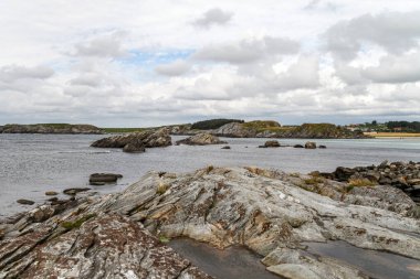 Norveç 'in arka planında bir su kütlesi olan kayalık bir kıyı şeridi. Kayalar büyük ve pürüzlü ve su sakin. Sahne huzurlu ve sakin, kayalıklarla