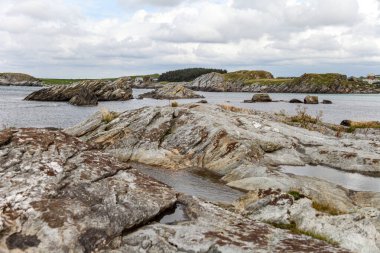 Norveç 'in arka planında bir su kütlesi olan kayalık bir kıyı şeridi. Kayalar büyük ve pürüzlü ve su sakin. Sahne huzurlu ve sakin, kayalıklarla