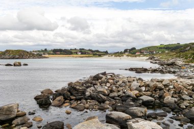 Norveç 'in arka planında bir su kütlesi olan kayalık bir kıyı şeridi. Su sakin ve kayalar kıyı boyunca dağılmış. Sahnenin huzurlu ve huzurlu bir atmosferi var.