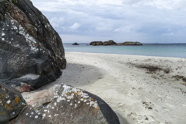 Norveç 'te kayalık bir plaj ve önünde büyük bir kaya var. Gökyüzü bulutlu ve su mavi.