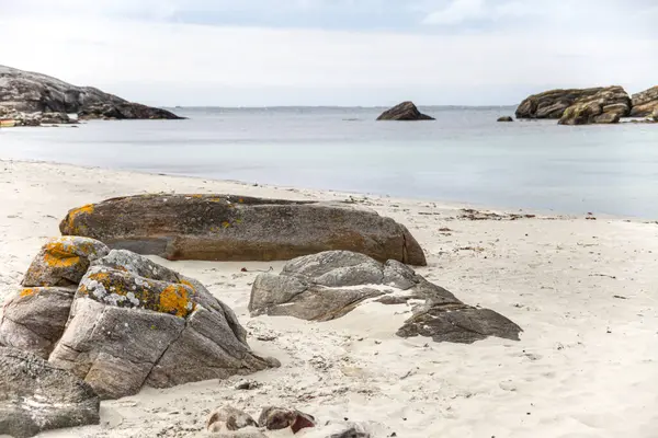 Norveç 'te kayalık bir plaj ve önünde büyük bir kaya var. Gökyüzü bulutlu ve su mavi.